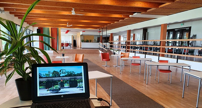 En laptop står uppställd på ett bord och i bakgrunden står flera enskilda bord med tillhörande stolar.