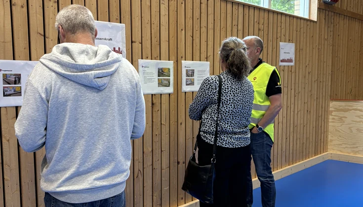 Tre personer tittar på information som sitter uppdatta på en vägg. 