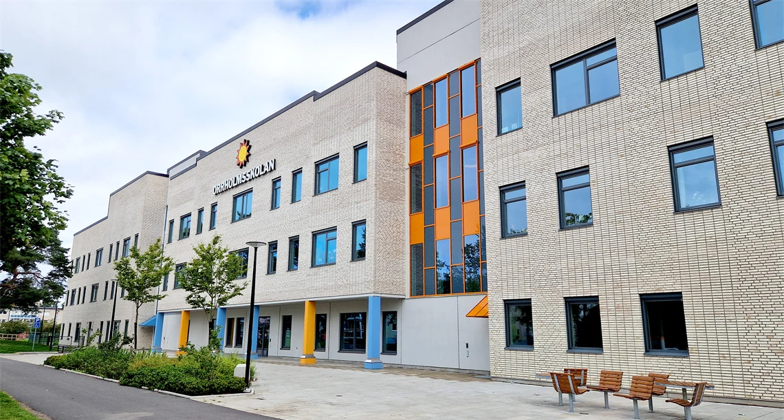 Orrholmsskolan sedd från framsidan, byggnad i ljust tegel i flera våningar med färgglada pelare i bottenplan