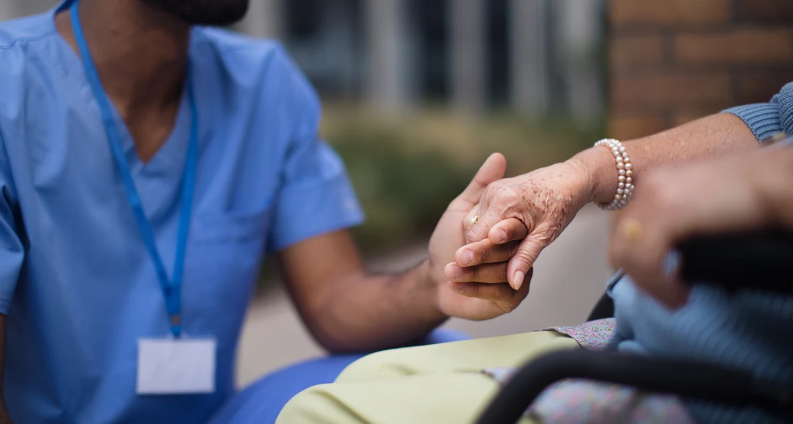 En person håller håller en person som sitter i rullstol i handen.