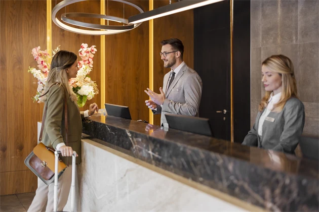 Två receptionister jobbar i en reception. Den ena hjälper en gäst att checka in.