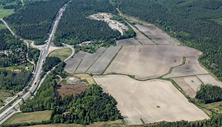Flygbild över motorväg, åkermark och skog.