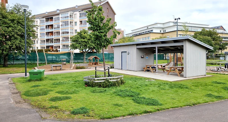 Utemijö på Orrholmens förskola, gräsmatta och en förrådsbyggnad med stolar och bänkar