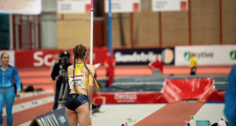 En tjej i gula sportkläder förbereder sig för att hoppa stavhopp.