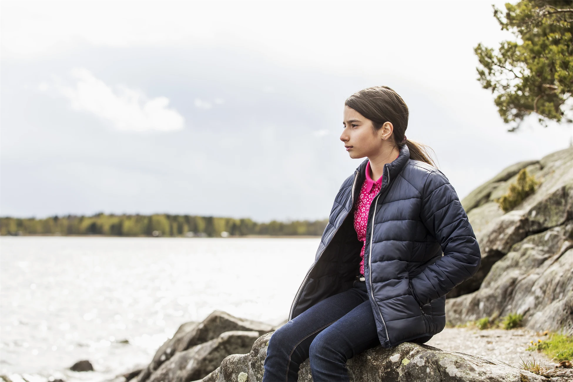 Flicka i blå jacka sitter på en klippa vid vatten