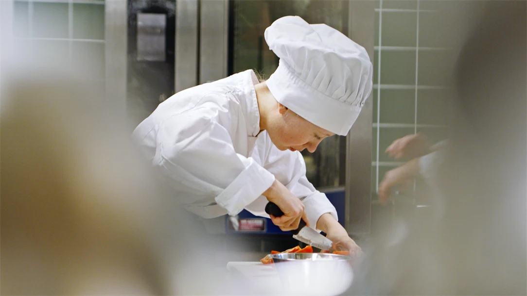 Elev står i kockkläder i ett kök och arbetar med att hacka grönsaker