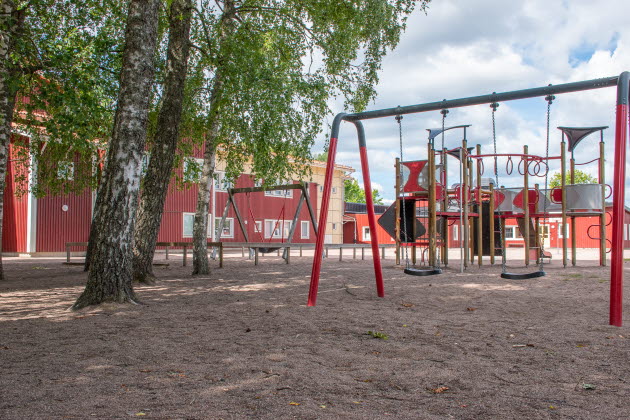 Lekplats med gungor utanför Stodeneskolans röda byggnad