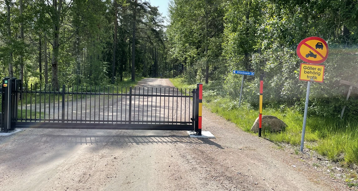 Grind som blockerar en grusväg. En passage finns vid sidan av grinden.