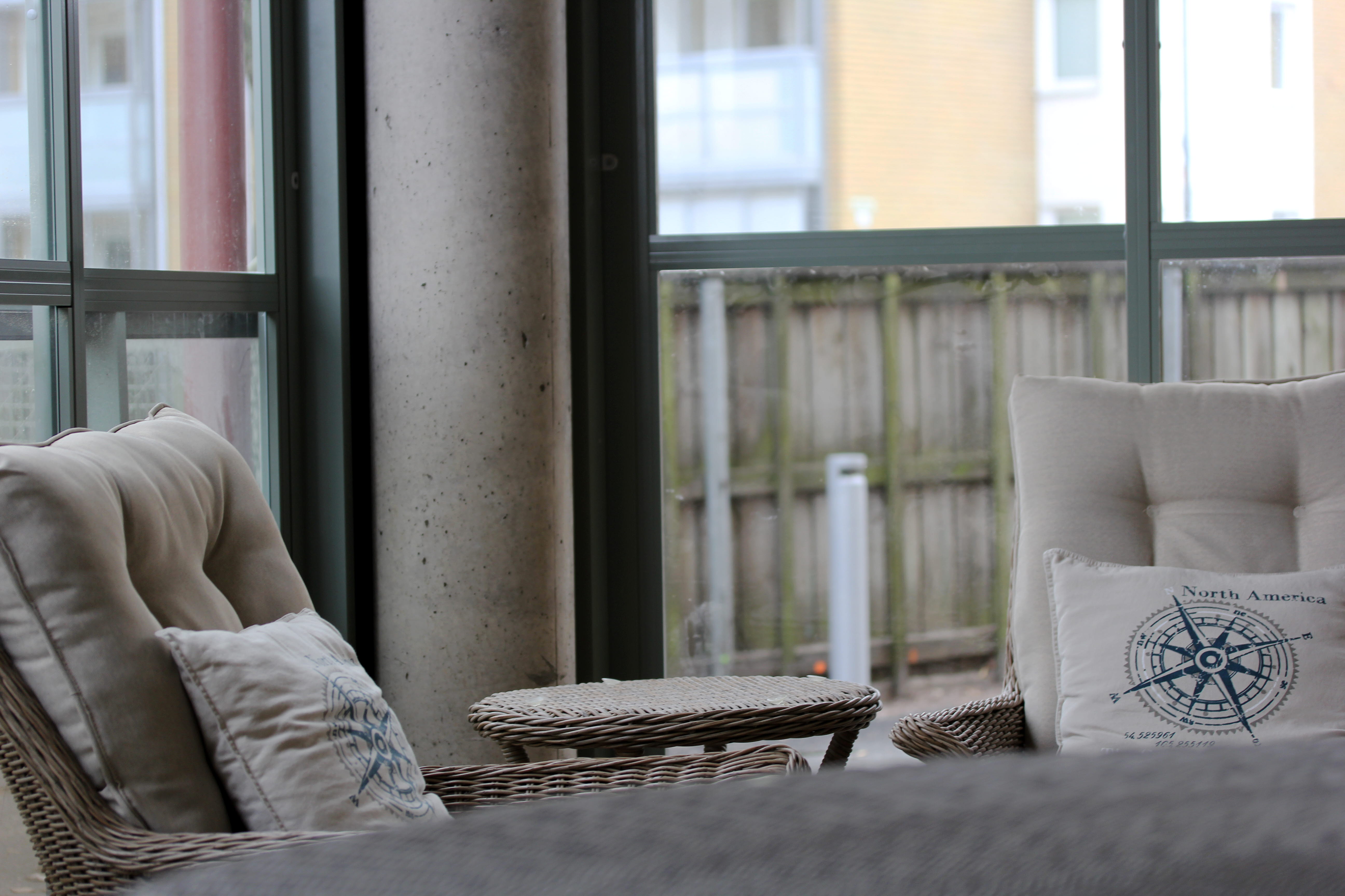 Två loungemöbler på en inglasad fasad. I bakgrunden skyms ett staket och lägenhetshus