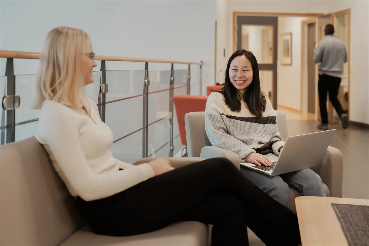 Två personer sitter vid ett bord. Den ena har en laptop i knät.