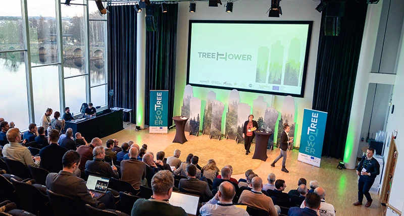 En sluttande möteslokal med flera stolsrader ner mot ett golv med stor skärm och två personer som leder ett möte.