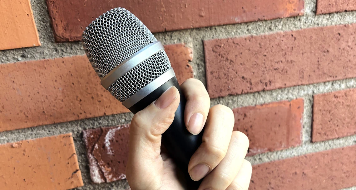 En hand som håller en mikrofon mot en tegelvägg