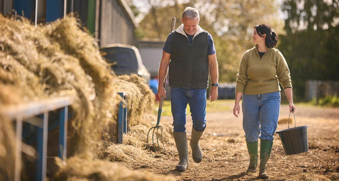 Två personer går bredvid en stor hög med hö.