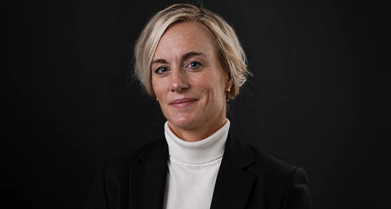 Porträtt mot mörk bakgrund av en person i svart kavaj och ljus polotröja.