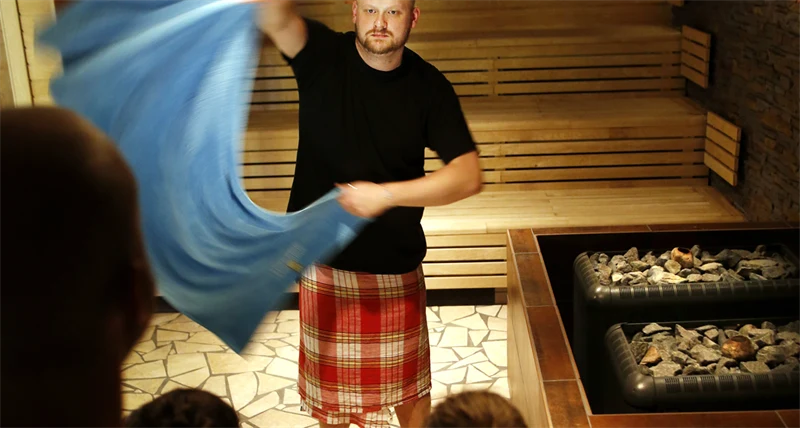 En bastuvärd vevar med en handduk i bastun.