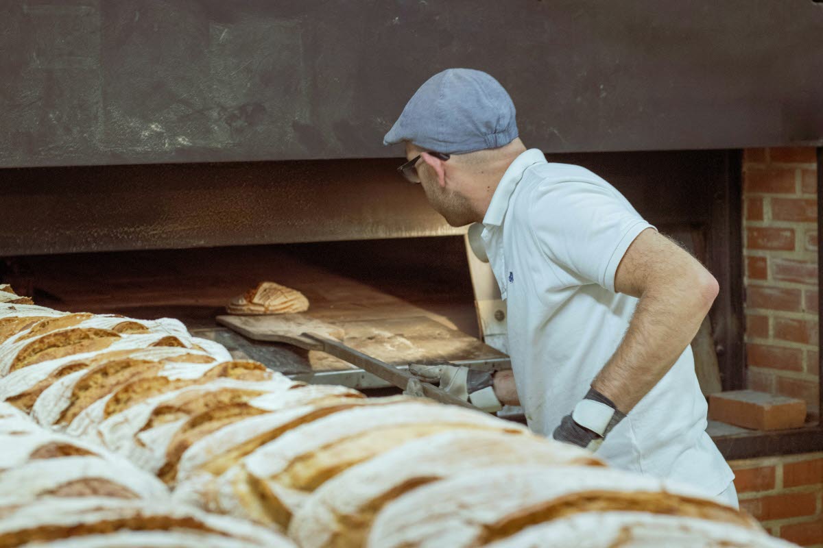 Person tar ut bröd ur en ugn i ett bageri
