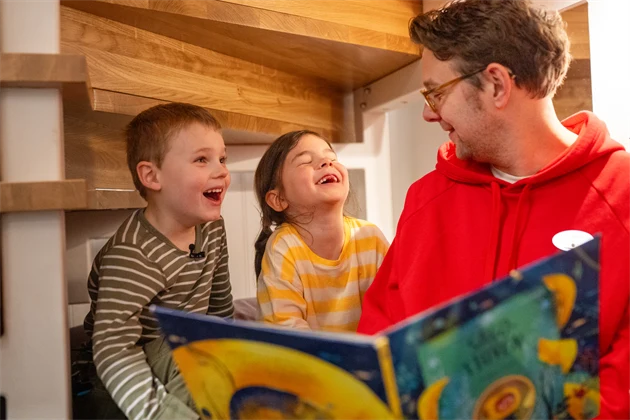 Man och två glada barn som läser i en bok