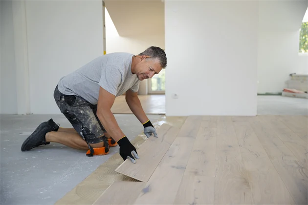 En golvläggare lägger ett trägolv i ett rum.