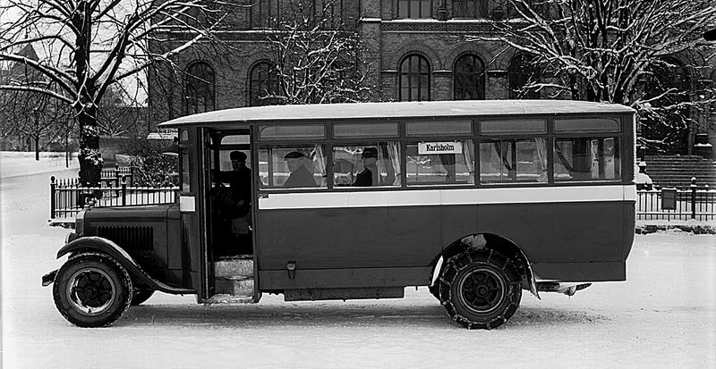 Fotografi av buss i linjetrafik i Karlstad på 1920-talet, parkerad utanför Allmänna Läroverket
