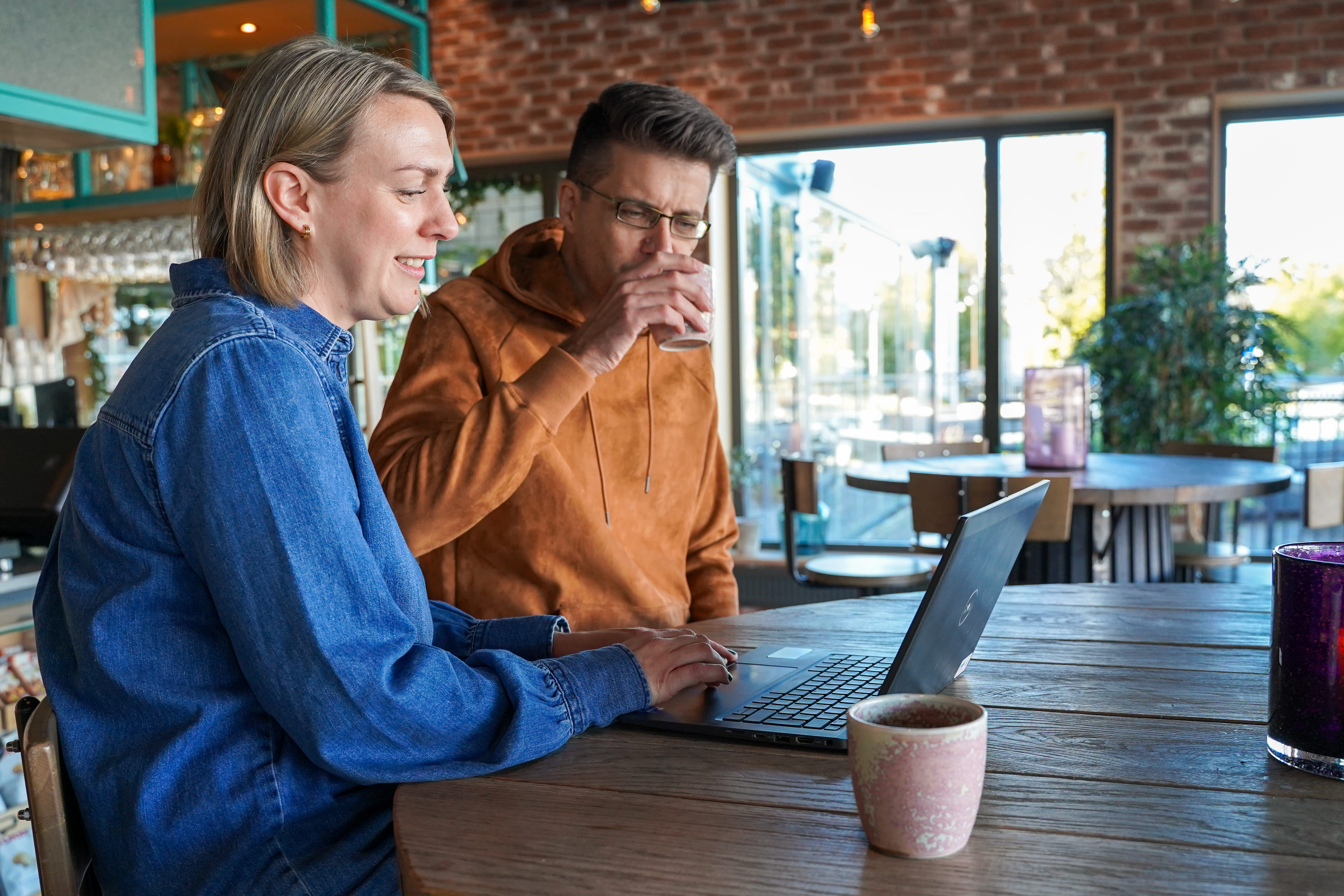Närbild två personer sitter och tittar på en dator och dricker kaffe på ett fik.