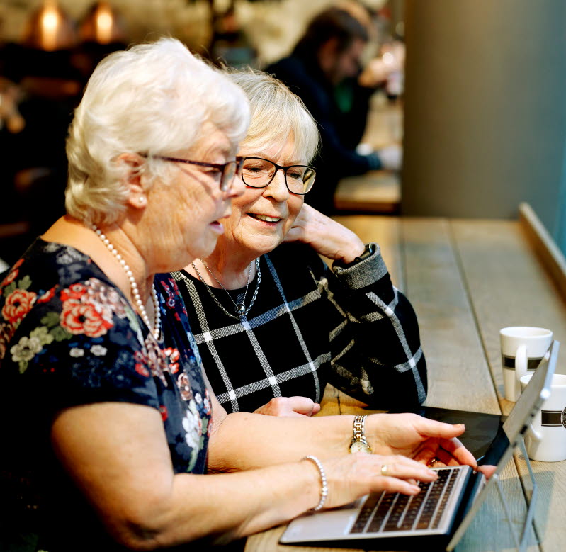 Två äldre kvinnor surfar på en dator tillsammans på ett café