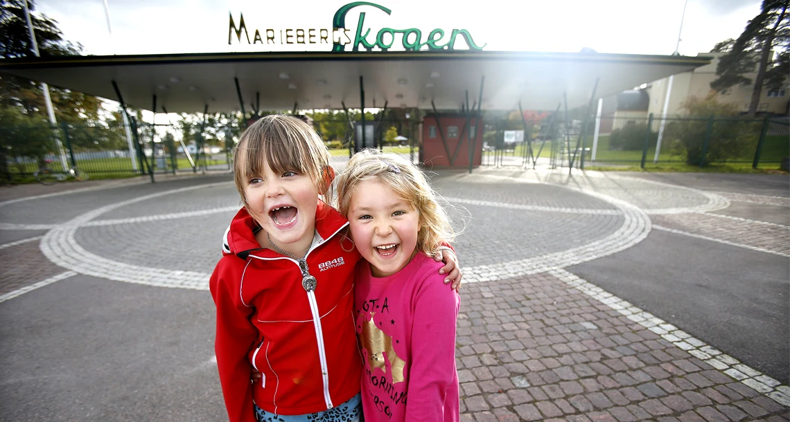 Två glada flickor vid huvudentrén till Mariebergsskogen. 