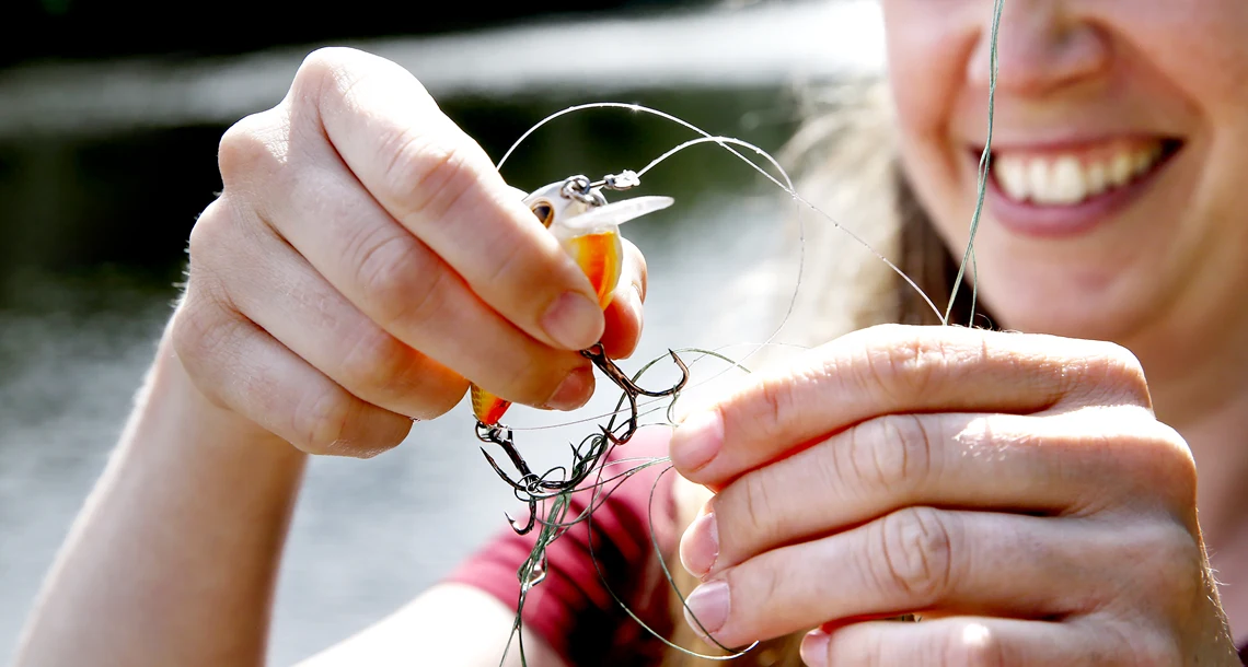 Kvinna ler och reder ut intrasslat fiskedrag ur fiskelina