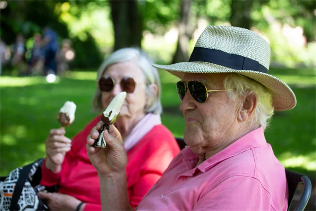 Man och kvinna sitter och äter glass, mannen har hatt på sig, de båda har solglasögon