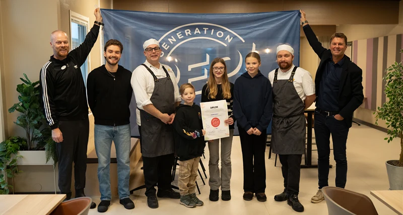 Personal och elever som håller upp flagga och diplom.