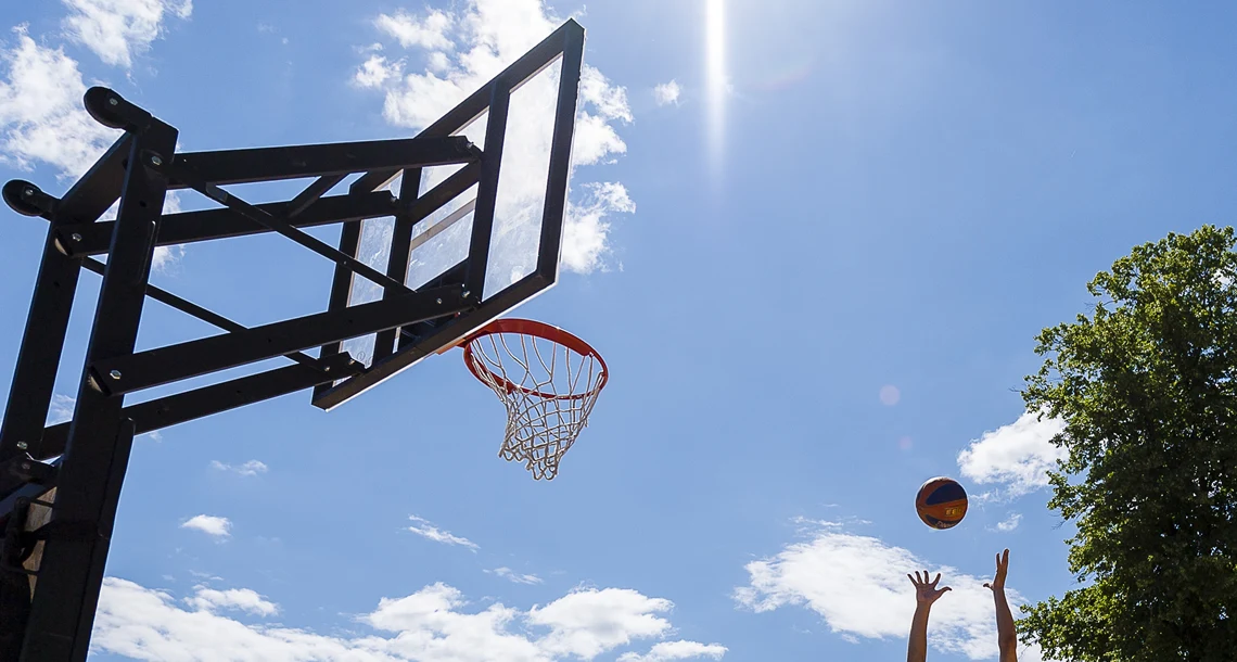 Händer kastar en basketboll i en korg mot en blå himmel