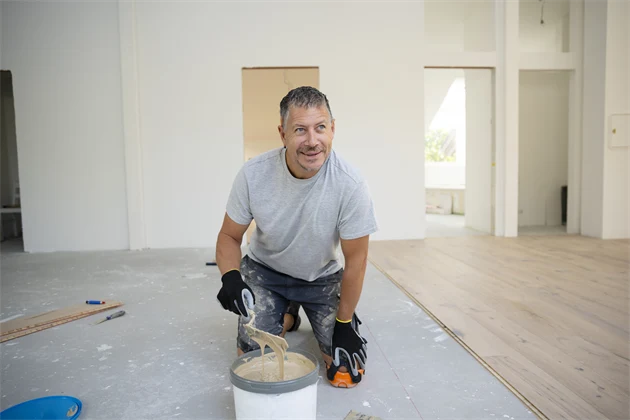 En golvläggare som lägger golv håller i en spatel med lim.