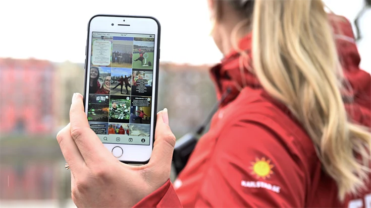 En fältarbetare håller upp en mobiltelefon där skärmen visar ett flöde i sociala smedier. 