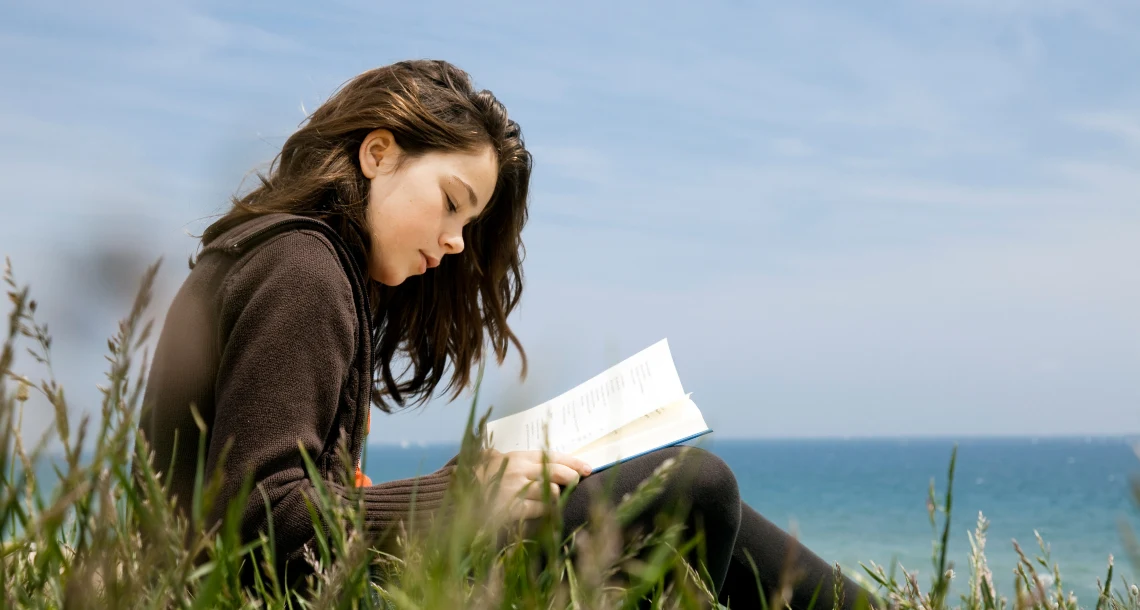 Flicka som läser utomhus vid havet