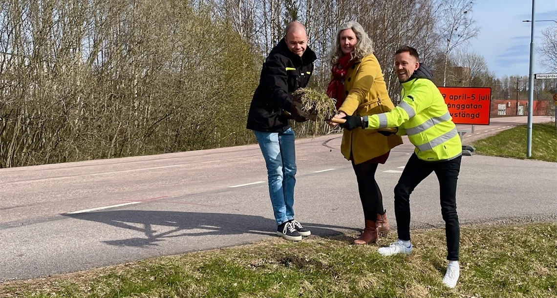 Tre personer tar ett spadtag vid en väg