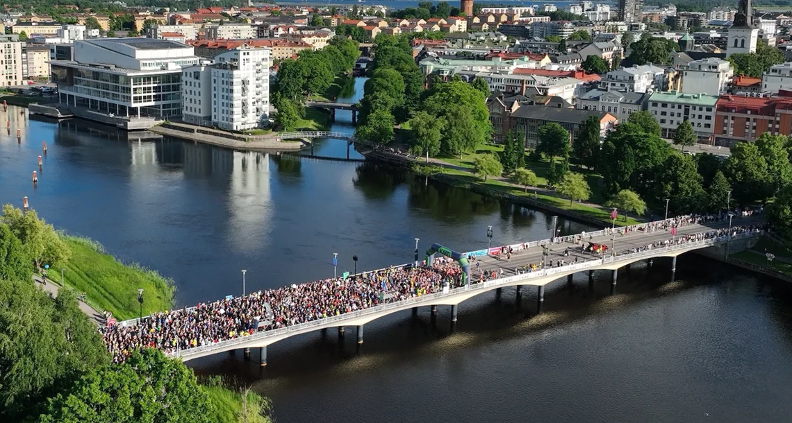 En drönarbild. Man ser en bro full med löpare som väntar på en start av ett lopp. Det är sommar, solen skiner och det är en strålande sommardag.