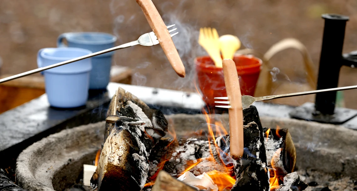 Två korvar på grillpinnar över öppen eld