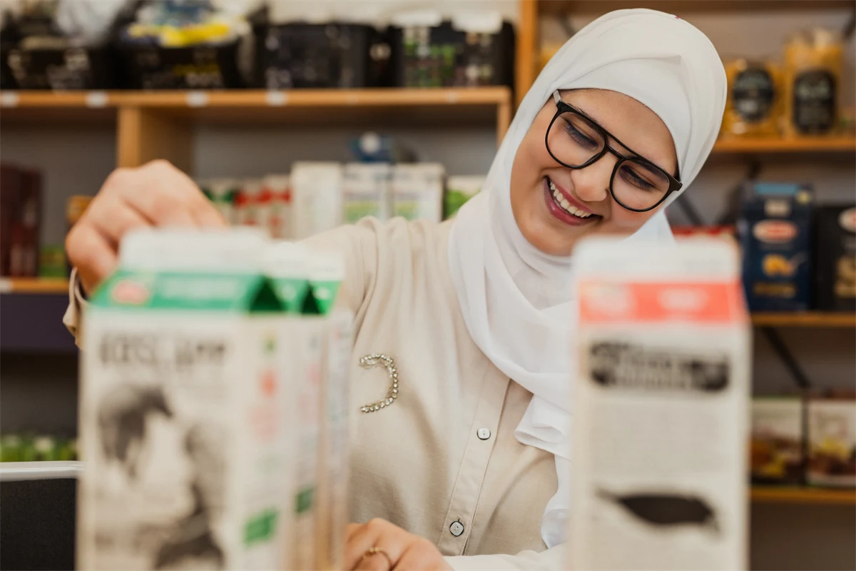 En gymnasieelev övar på att ställa fram varor i en butik och skrattar.