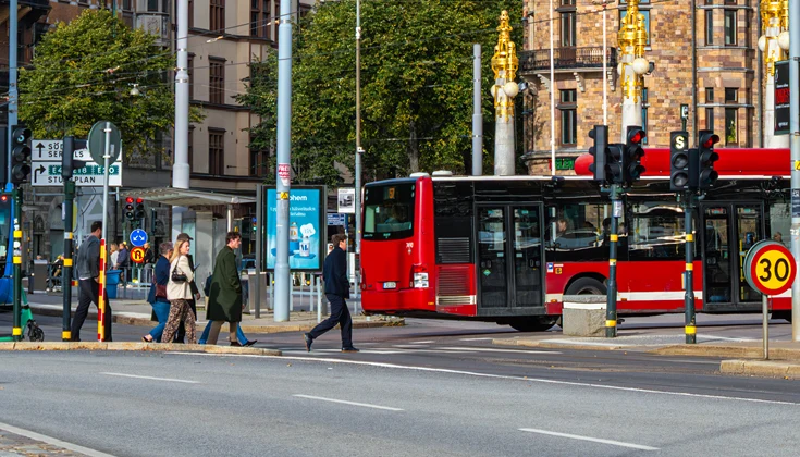 Bussar, bildar och människor på ett övergångställe i en storstad.