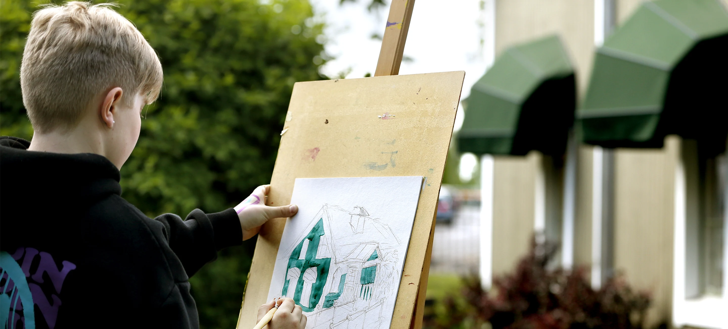 Pojke som målar ett grönt hus på ett straffli utomhus