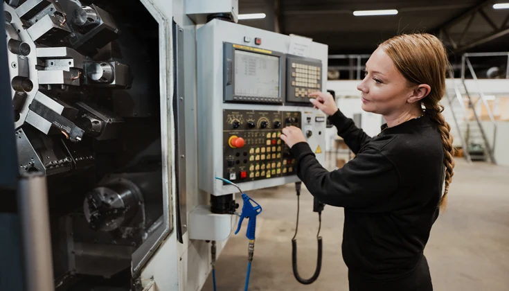 En person använder en CNC-maskin i en verkstad.