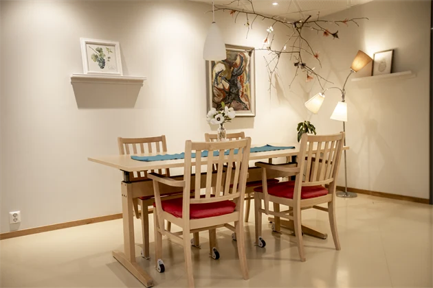 Matbord och stolar i trä. På den vita bakomliggande väggen finns konst.