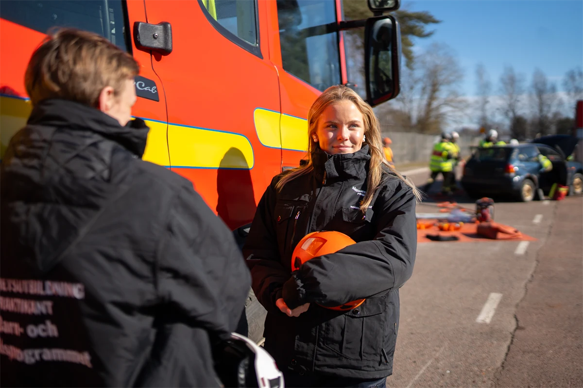 Två ungdomar står framför en parkerad brandbil.
