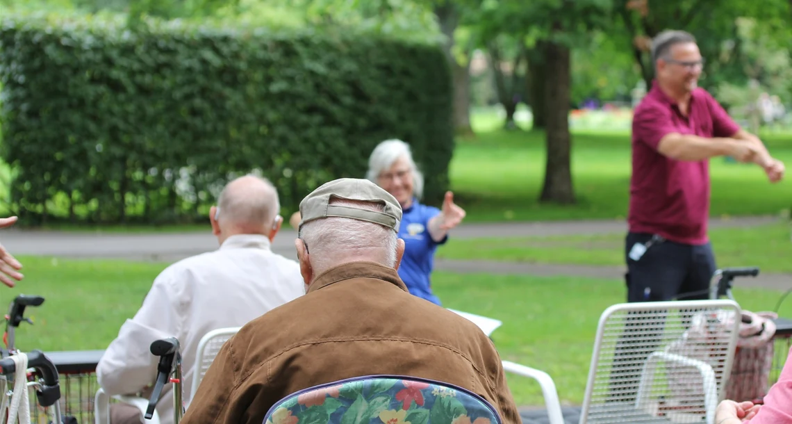 Personer sitter i en park. Framför dem är personal från Karlstads kommun som visar övningar.