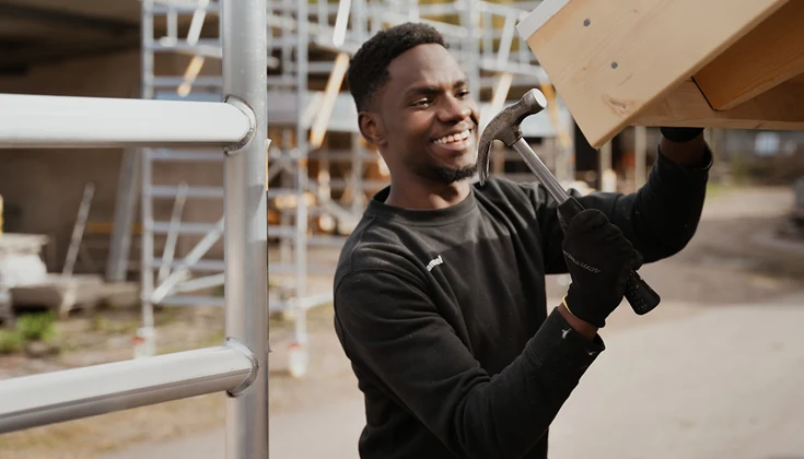 Elev i byggmiljö utomhus, spikar på taket till en lekstuga.