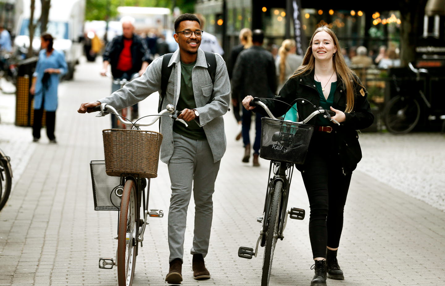 Två studenter går gatan fram med sina cyklar.