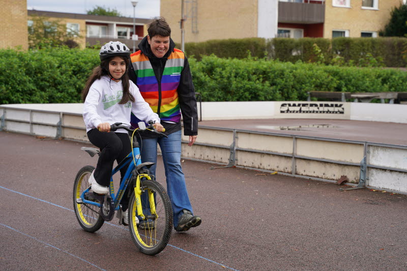 Elev på cykel tillsammans med pedagog som hjälper till att hålla balansen.