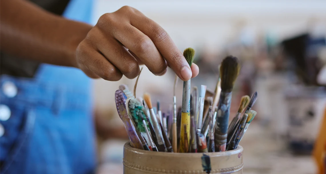 En person sträcker sig efter penslar i en burk.