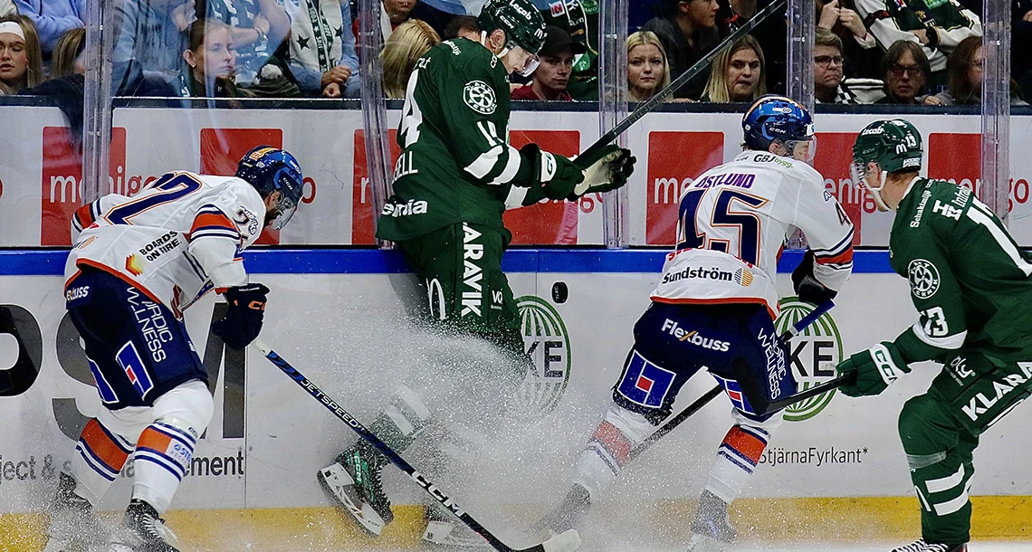 Två olika hockeylag i grönt och vitt spelar om pucken med publik i bakgrunden.