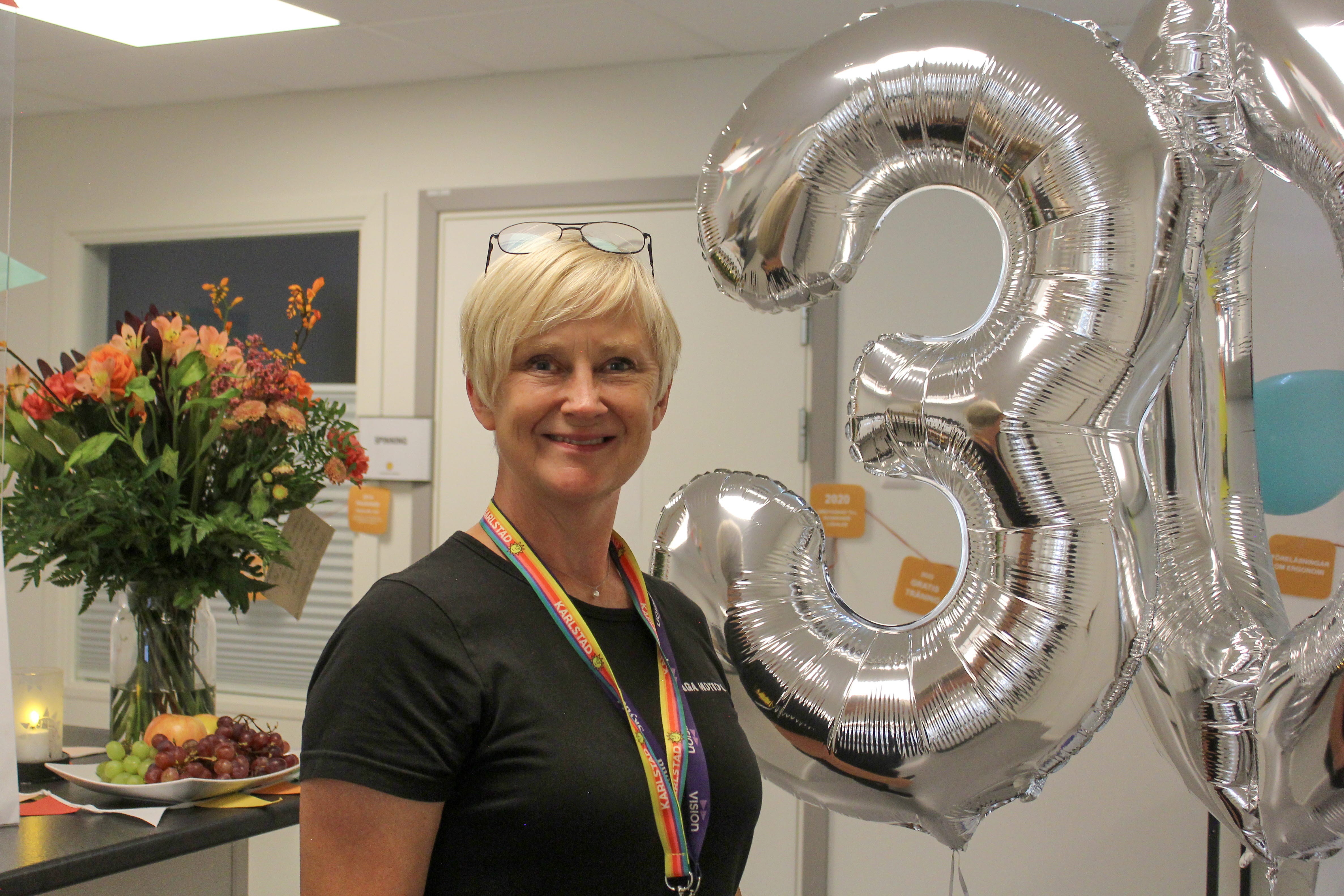 Glad tjej ler och tittar in i kameran. Brevid henne hänger ballonger i formen av en trea och en nolla.