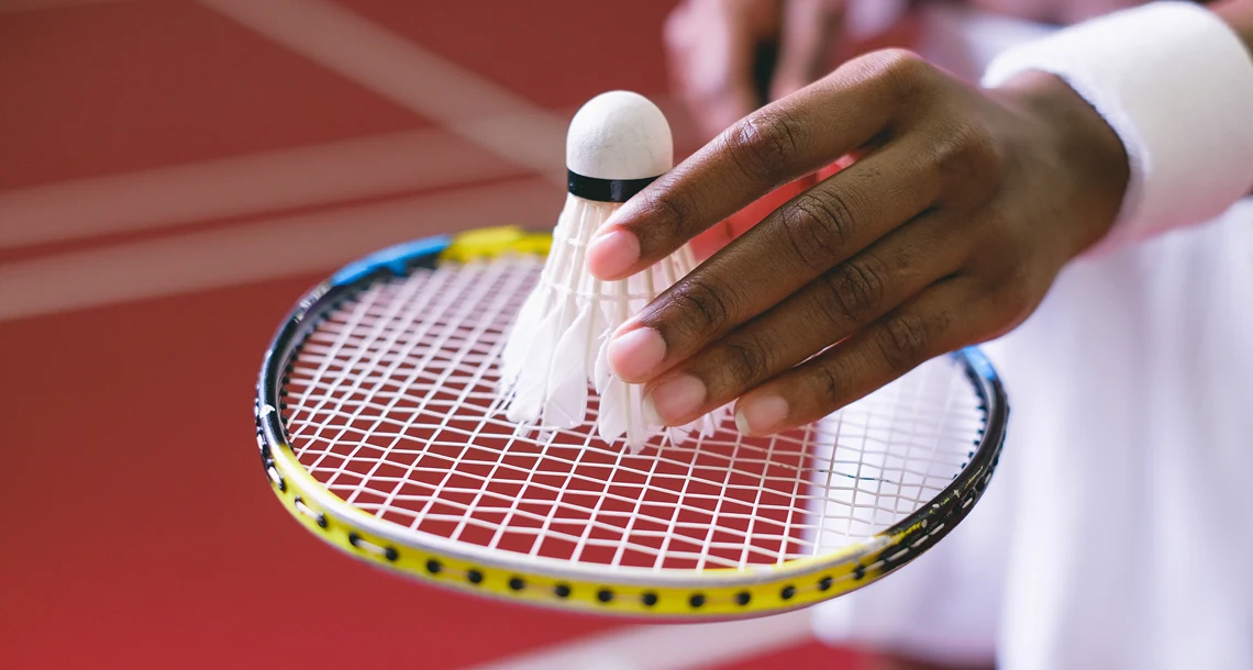 Händer som håller ett badmintonrack och en badmintonboll